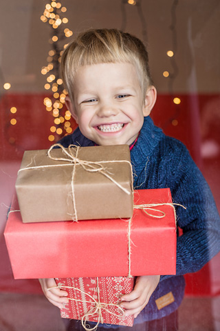 Young boy in blue sweater smiles as he carries Christmas presents