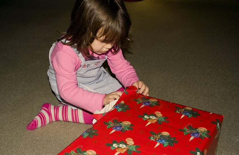 Young girl, sitting on the floor, opening Christmas present
